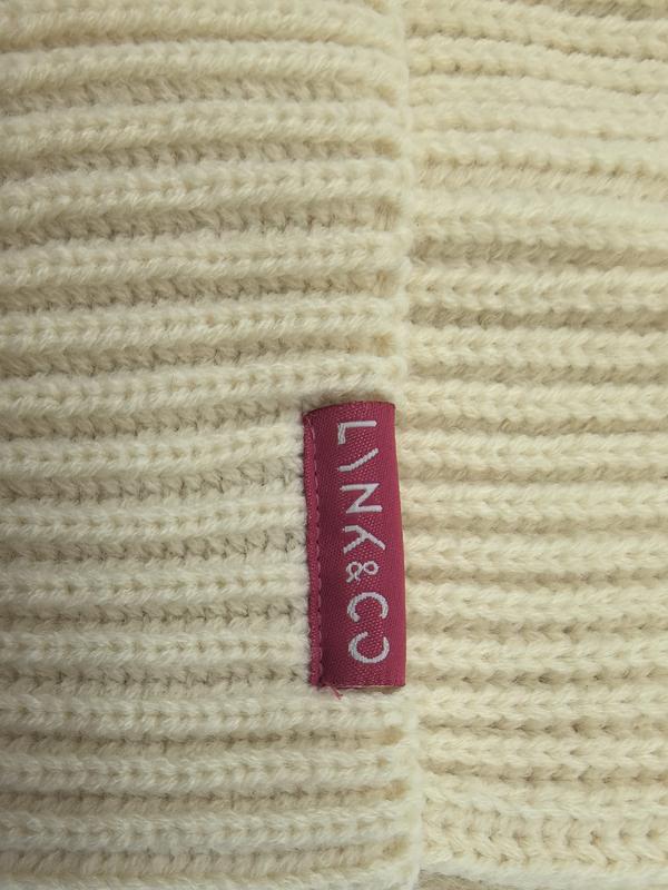 Close-up of a cream chunky ribbed knit blanket featuring a magenta woven brand label sewn into the fabric