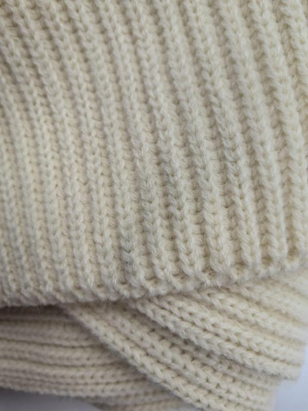 Close-up of a chunky ribbed knit blanket in cream ivory color showing detailed stitch texture and folded layers