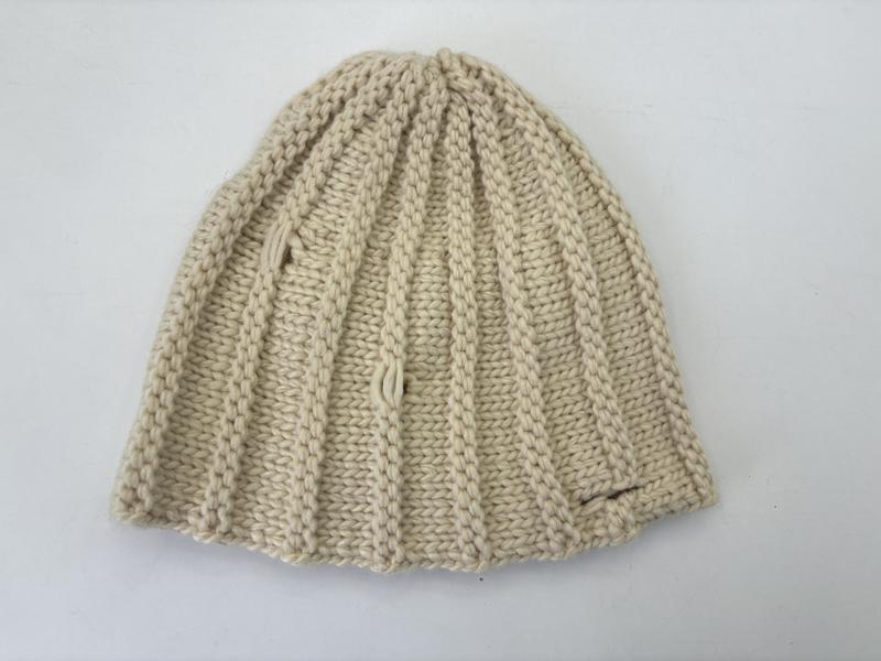 Flat lay of a cream chunky ribbed knit beanie hat in ivory natural yarn, folded to show textured stitch pattern