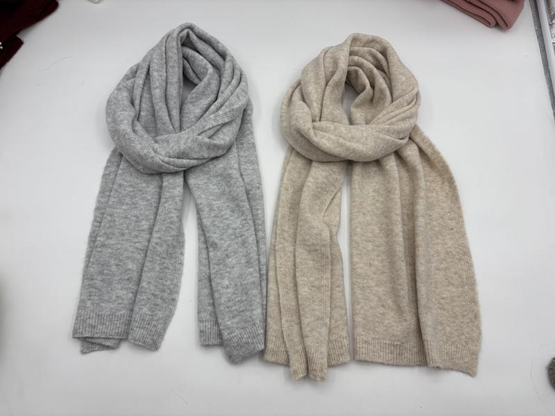 Two soft knit scarves laid flat, one light grey and one beige, with ribbed ends and cozy wrapped styling