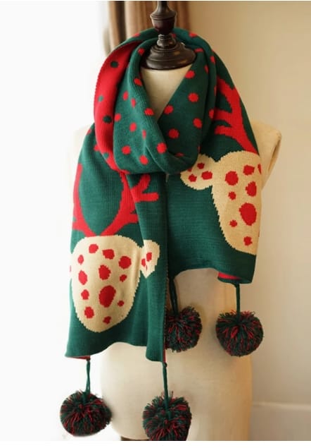 Green knitted holiday scarf with reindeer and red polka dot pattern, displayed on mannequin with decorative pom-pom fringe ends