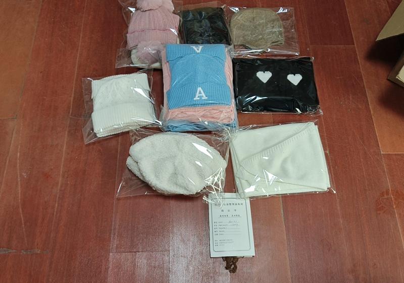 Multiple packaged knit beanies and scarves in pink, blue, black, cream, and tan colors displayed on wooden floor with product card