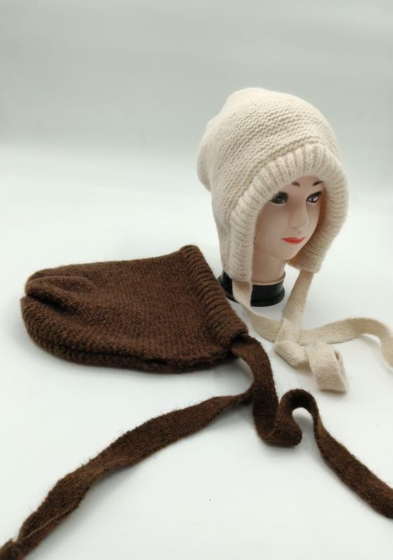 Cream chunky knit earflap beanie on mannequin head beside a brown knit bonnet hat with long tie straps on white background