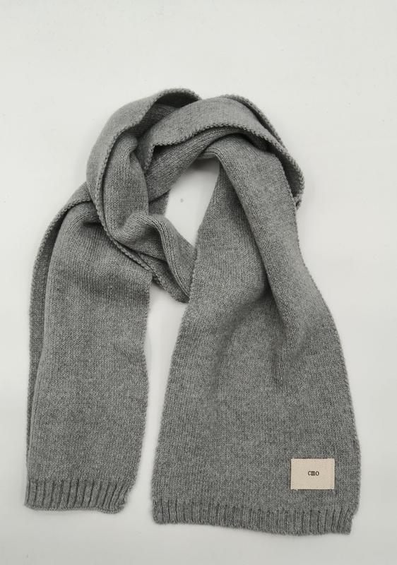 Heather grey knitted scarf with ribbed edges and woven label, loosely draped on white background