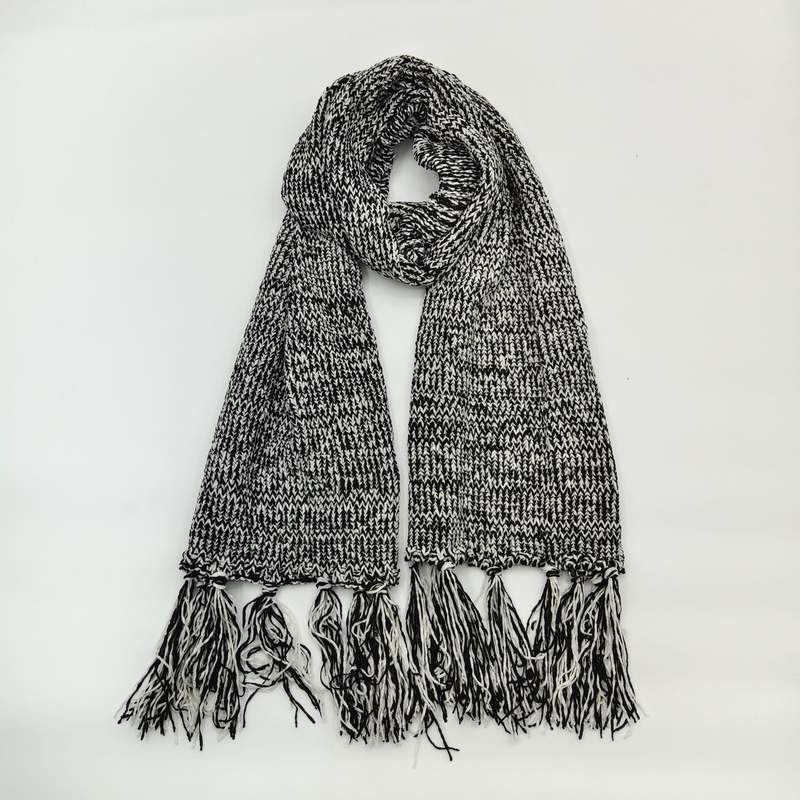 Black and white marled chunky knit winter scarf with long tassel fringe ends, looped and laid flat on white background