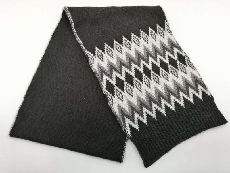 Folded dark charcoal knit scarf with white and grey Fair Isle Nordic zigzag pattern and ribbed hem ends