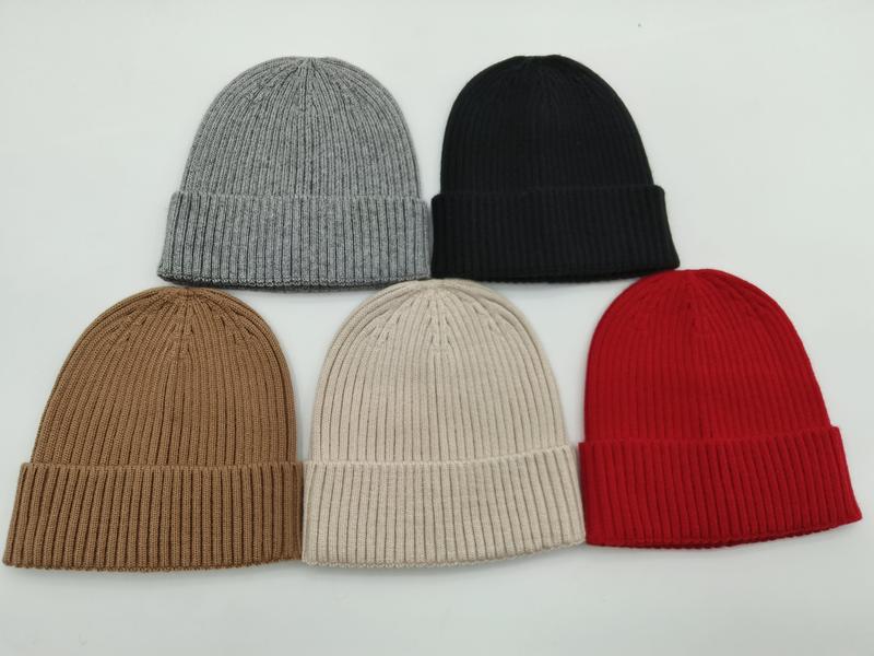Five ribbed knit cuffed beanies in grey, black, camel, cream, and red arranged on white background