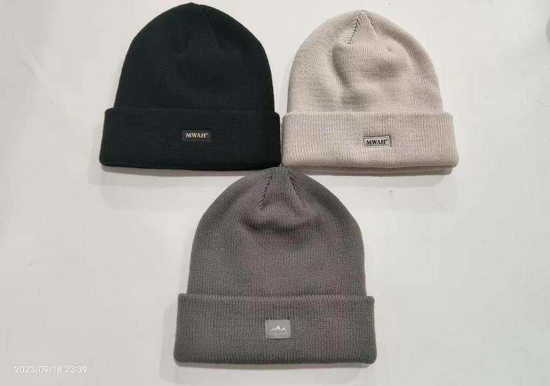 Three cuffed knit beanies laid flat in black, light beige, and charcoal grey with small woven brand labels on the cuff