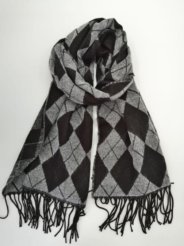 Black and grey argyle diamond pattern woven scarf with black tassel fringe ends, folded and draped on white background