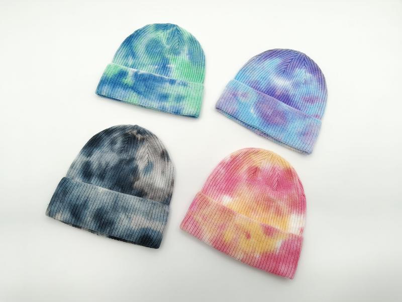 Four tie-dye ribbed knit beanies in blue-green, purple-blue, dark grey, and pink-yellow colorways on white background