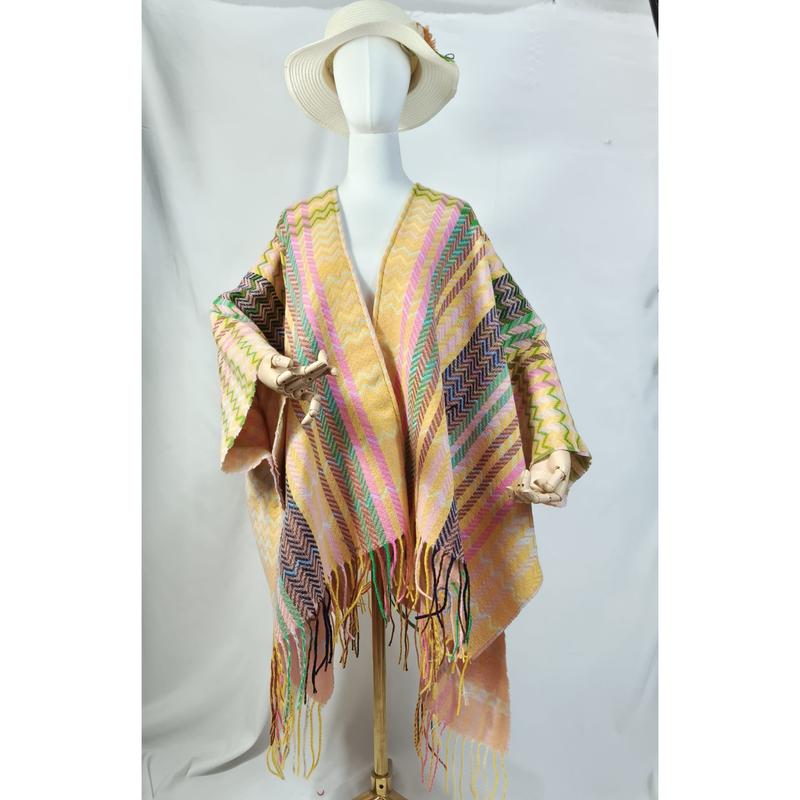 Mannequin wearing a multicolor woven poncho shawl with zigzag stripes in pink, yellow, green, and fringe hem, styled with white sun hat