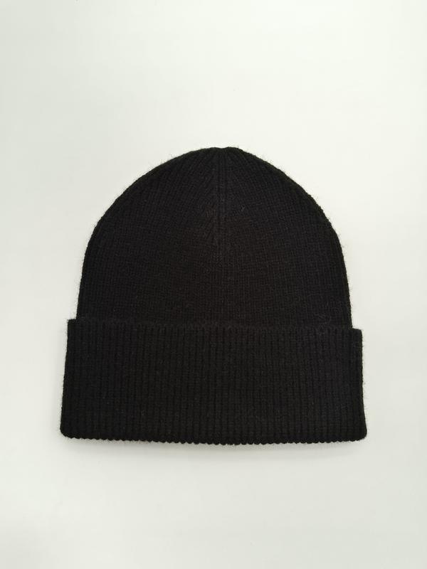Black ribbed knit beanie with folded cuff laid flat on white background, soft wool winter hat