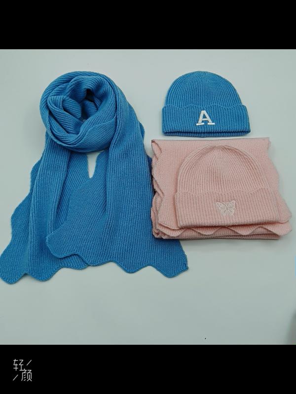 Blue knit scarf and beanie with letter A embroidery beside pink knit hat and scarf set with butterfly detail on white surface