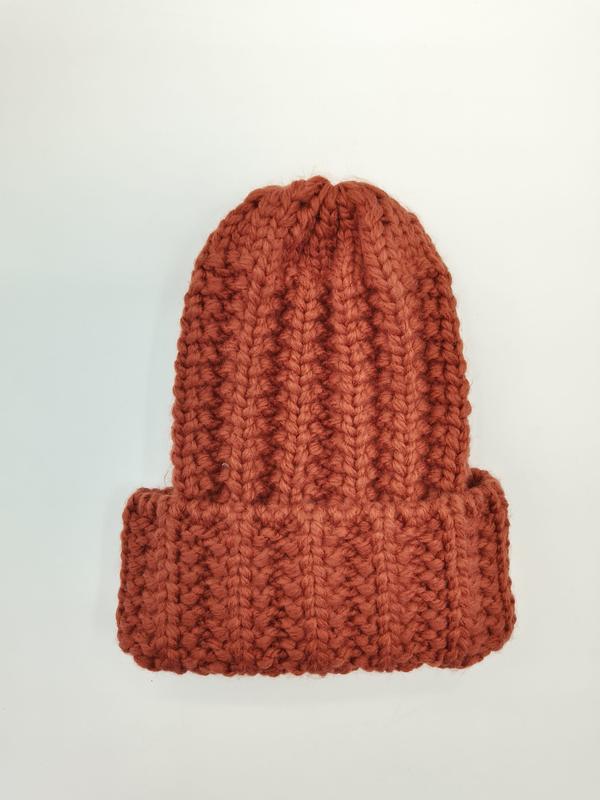 Rust orange chunky ribbed knit beanie hat with folded cuff, laid flat on white background, handmade wool texture