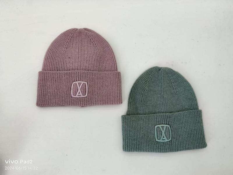 Two ribbed knit cuffed beanies in mauve pink and sage green with embossed logo patch, laid flat on white surface