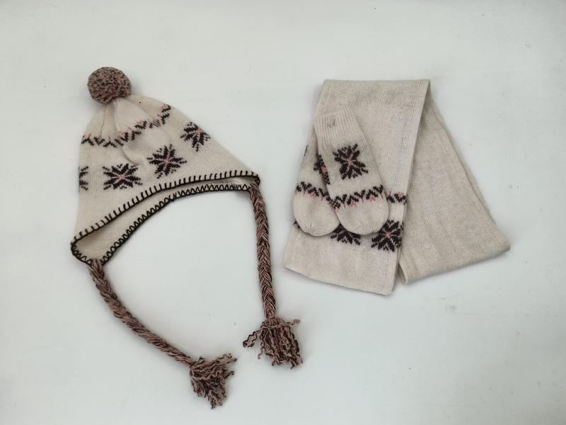 Cream knit winter set with Nordic snowflake pattern including earflap pom-pom hat with braided tassels, mittens, and scarf
