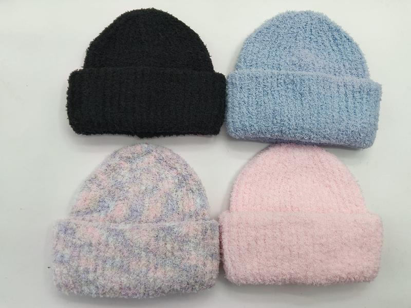 Four fluffy knit cuffed beanies in black, light blue, pastel tie-dye, and pink laid flat on white background
