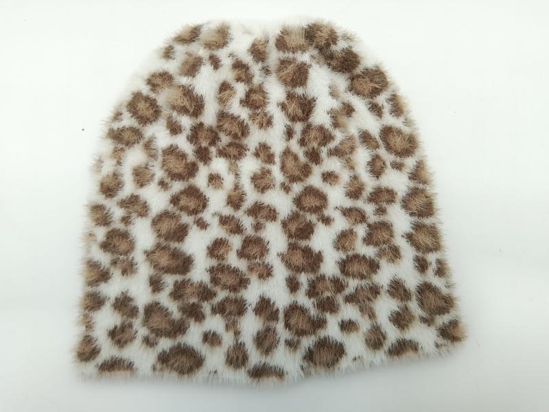 Soft white faux fur beanie hat with brown leopard print spots laid flat on white background