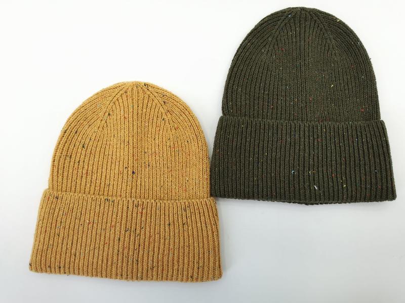 Two ribbed knit cuffed beanies with multicolor fleck detail in mustard yellow and olive green, laid flat on white background