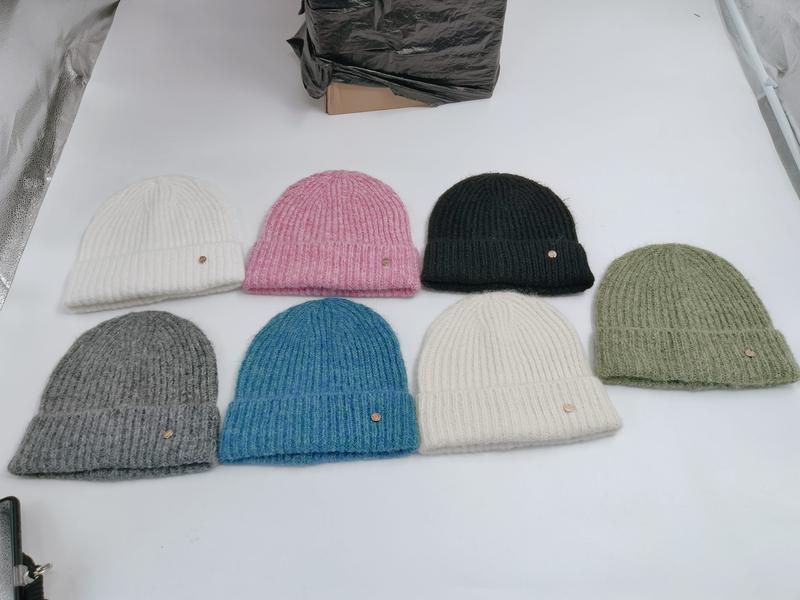 Seven ribbed knit beanies in white, pink, dark green, sage, gray, blue, and cream laid flat on white surface