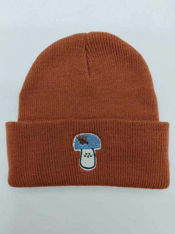 Rust orange ribbed knit cuffed beanie hat with blue and white embroidered mushroom patch on folded brim
