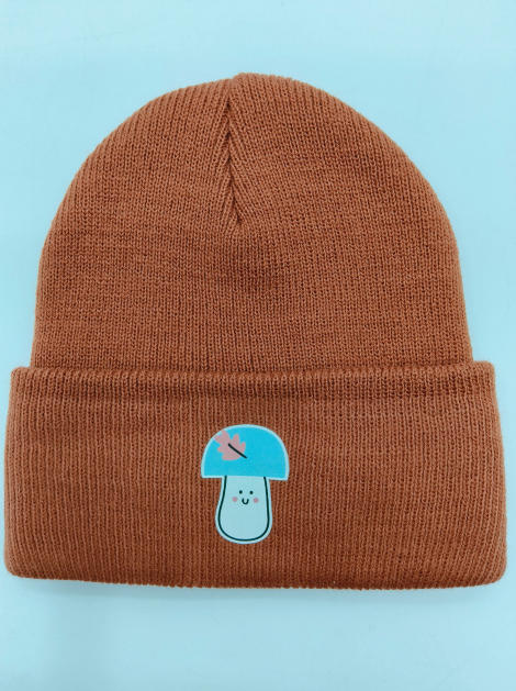 Rust brown ribbed knit cuffed beanie hat featuring a kawaii blue mushroom character patch on the fold