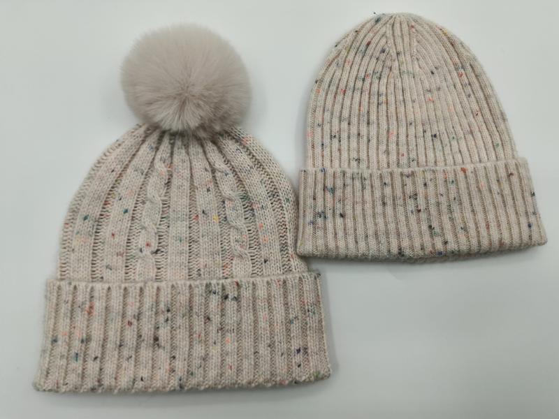 Two cream speckled knit winter beanies side by side, one with faux fur pom-pom and cable knit, one plain ribbed style