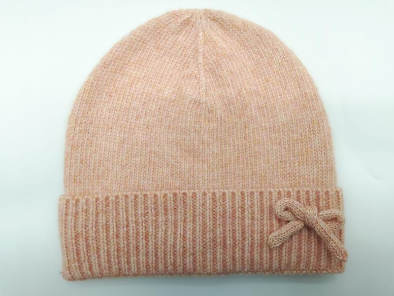 Soft peach marl knit beanie hat with folded ribbed cuff and decorative knitted bow accent on light background