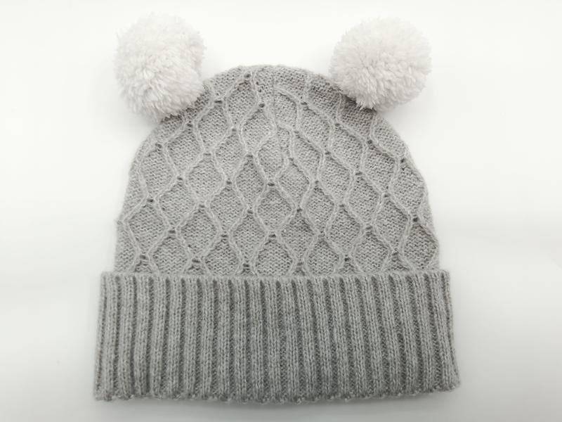 Grey cable knit baby winter beanie hat with two fluffy white pom poms and ribbed cuff, laid flat on white background