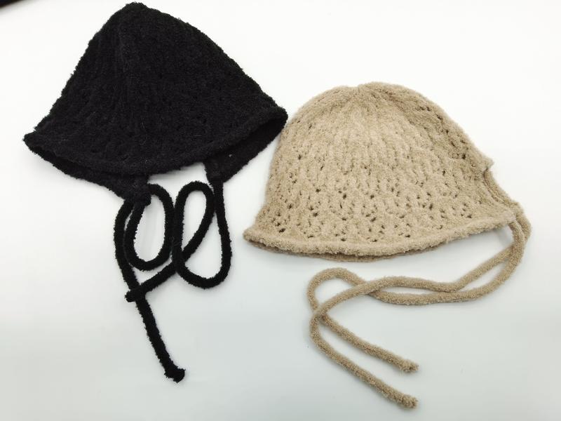 Two handmade crochet knit bucket hats with tie strings laid flat, one black and one beige, showing open lace pattern texture