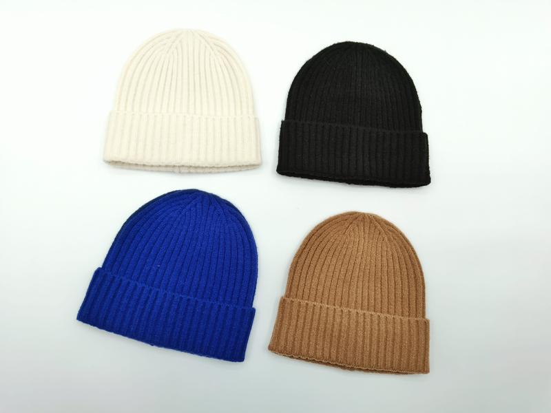 Four ribbed knit cuffed beanies in cream, black, cobalt blue, and camel arranged on white background