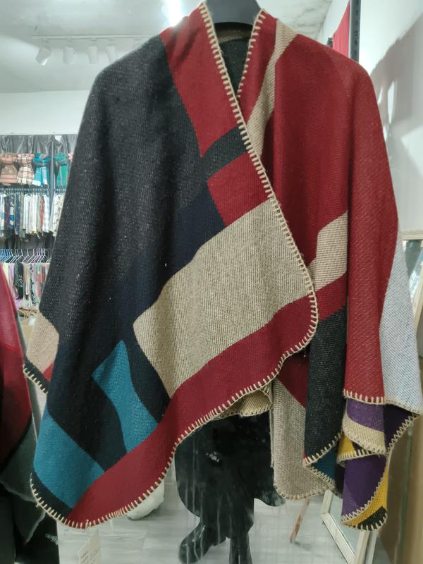 Oversized wool blend poncho wrap with geometric color block pattern in charcoal, red, teal, and beige with blanket stitch edges
