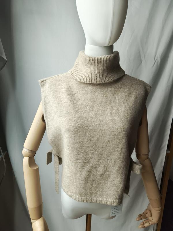 Beige sleeveless turtleneck knit sweater vest with side tie details displayed on a dress mannequin